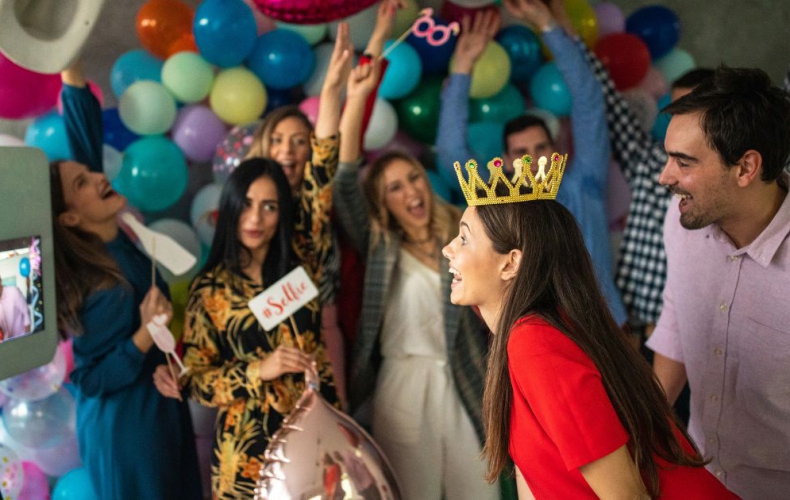 A couple taking photos at a digital photo booth surrounded by friends